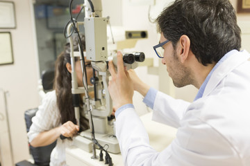Photo of patient looking at medical apparatus during vision checking in ophthalmological laboratory with experienced ophthalmologist..Trying to improve vision in modern oculist' cabinet.