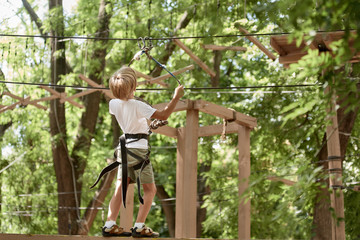 Naklejka na ściany i meble Portrait of little happy boy climbing in adventure park