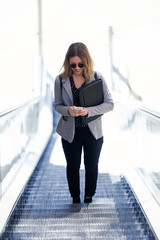 Pretty young business woman using her mobile phone in the mechanical stairs.