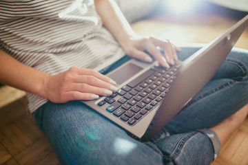 Young female student with laptop on her legs while sitting on the floor.