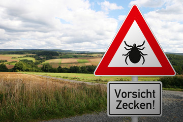 Schild warnt vor Zeckengefahr im Risikogebiet - mit Landschaft im Hintergrund