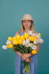 Beautiful girl in the blue dress with flowers tulips in hands on a light blue background. Beauty, fashion concept. Spring and summer holidays.