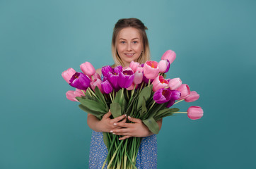 Smiling woman with bouquet of pink and purple tulips. Smiling woman with bunch of flowers in her hands in blue dress. Summer and spring concept. Isolated on blue background