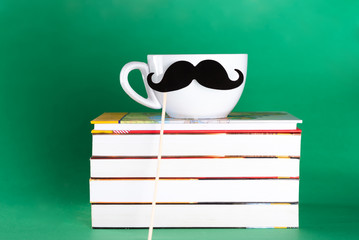 Books, white cup and cute mustache on green background.Happy fathers day, back to school, concept.