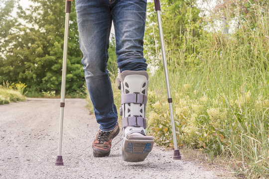 Mann l&auml;uft mit einer Orthese und Gehhilfen &uuml;ber einen Feldweg