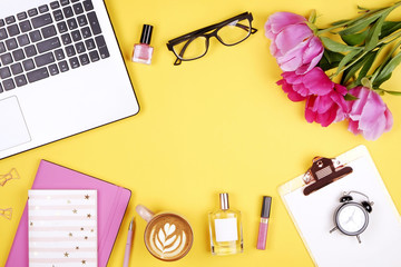 Feminine desktop, close up, laptop keyboard, blank clipboard, coffee, peony flowers, perfume, lip gloss. Flat lay composition, computer, cappuccino cup, glasses eye wear, yellow background. Copy space