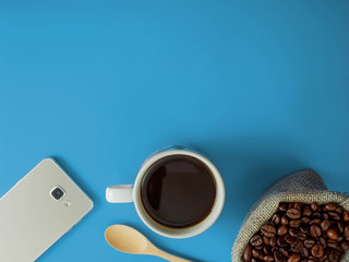 Flat lay a cup of coffee and smartphone on blue desk with copy space