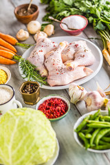 Raw chicken legs with assortment spices and vegetables.