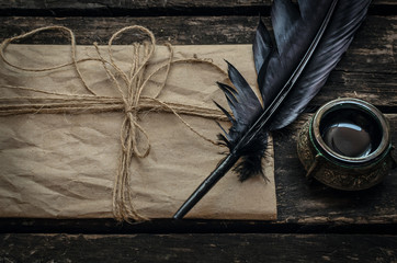 Old vintage letter envelope, feather pen and inkwell on aged wooden table board background.