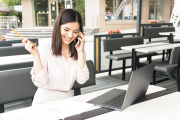 Young pretty woman speaking on mobile phone and sitting in cafe with notebook.