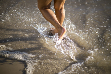 Close-up abstract image of feet splashing through waves lapping at a sandy beach