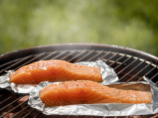 Cooking salmon fillets on a barbecue outdoors. Fillets are on foil, smoke and blurred grass...