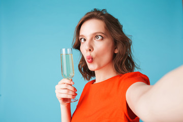 Portrait of young lady in dress standing with champagne and taking cute photos on over pink background