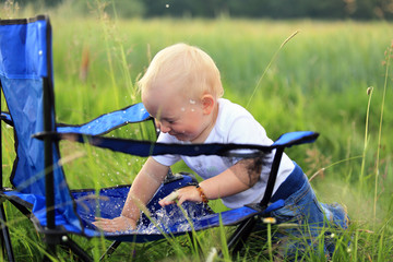 Małe dziecko chlapie się wodą na fotelu na łące. - obrazy, fototapety, plakaty