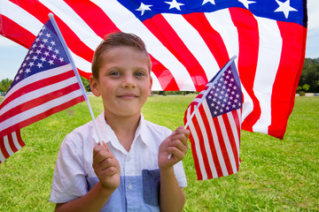 Little boy holding american flags outdoors on US Independence day, July 4th
