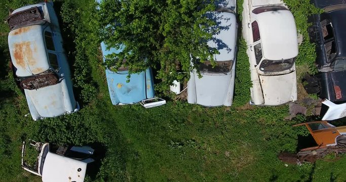 Aerial view of broken rusty cars amidst greenery, the field lined with old machines for disassemble