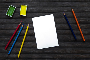 Blank card and paint and crayon flat lay on rustic wooden background. Empty postcard and art supplies.