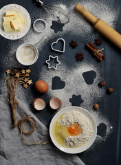 Fototapeta na wymiar A set for making cookies. Flour and egg in a bowl, butter, sugar, cookie shapes, nutmeg, cinnamon, anise, rolling pin, whisk for whipping. Dark background. Vertical orientation of the frame. Close-up.