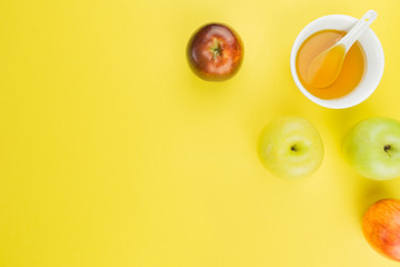 Rosh Hashanah, apples and cup of honey on yellow background. free space for text