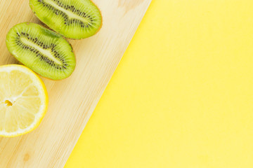 Lemon and kiwi cut in half on wooden desk. Yellow free space for text. center compisition