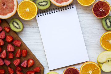 Top view, colorful fruit pattern of apple, grapefruit, kiwi, strawberries and orange on a white wooden background. From above. Flat lay.