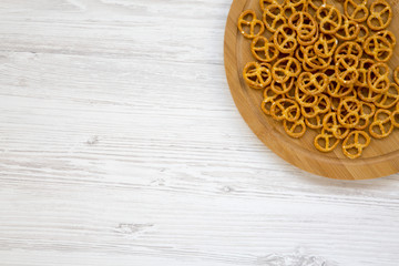 Salt pretzels on round bamboo board on white wooden background, top view. Copy space.