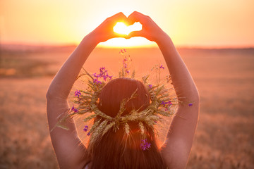 girl on wheat field making heart symbol at sunset