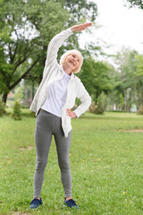 Fototapeta premium elderly sportswoman stretching on green lawn in park