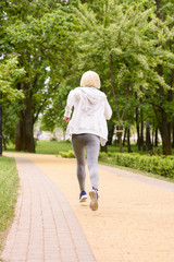 back view of sportive woman with grey hair jogging in park