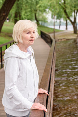 lonely senior woman standing near railings in park