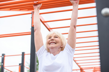 cheerful senior woman exercising on sports ground