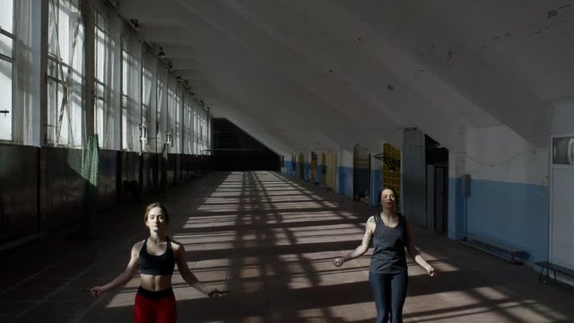 Crane shot with tilt down of athletic sportswomen in fitness clothes jumping rope in empty gym