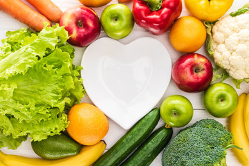 top view of fresh fruits with vegetables and empty heart shaped plate on wooden table