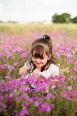 Fototapeta na wymiar Little girl with dark hair in a purple flower field during the evening golden light in the summer