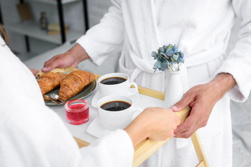 cropped view of couple holding tray with croissants and coffee for breakfast