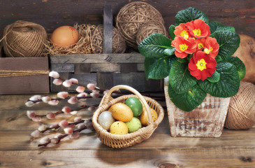 Basket of Easter eggs, red primrose flowers in flower pot on wooden table
