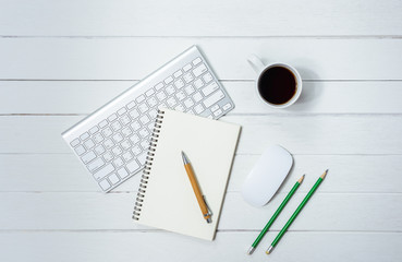 Wooden White office desk table with cup of coffee, Notebook, Pen on it.