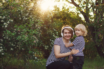Fototapeta premium Mother and son in striped T-shirts. Woman listening to music on headphones. Boy stands next to her. Family time together.