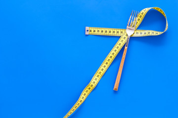 Proper nutrition for slimming. Fork and knife with wound measuring tape on blue background top view...