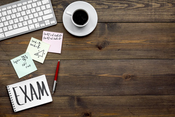 Preparing for the exam. Word Exam written in notebook on student's desk with computer, cup of coffee, cheat sheets on dark wooden backgrond top view space for text