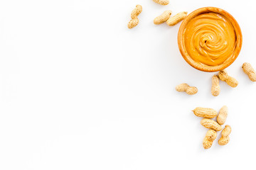 Product for hearty breakfast. High-calorie product. Peanut butter in bowl near nuts in shell on white background top view space for text