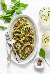 Spinach, zucchini, green peas, garden herbs fritters and white wine on a light background, top view. Tasty appetizers, snack, tapas. Flat lay