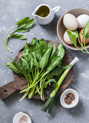 Ingredients for green shakshuka - fresh spinach, garlic, ramson and organic farm eggs on grey background, top view