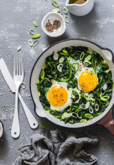 Green shakshuka. Fried eggs with fresh spinach, ramson, leek in a pan on a gray background, top view