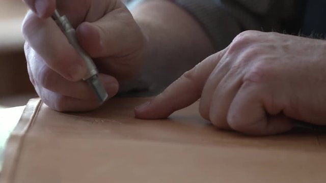 A leatherworker uses a metal tool to carve a design into a piece of leather.