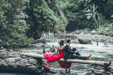 A beautiful young honeymoon couple posing on the river in the jungle of Bali island.