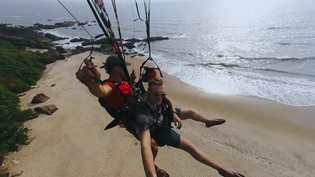 Two men flying on paraplane above rocky mountain and taking off on ocean beach