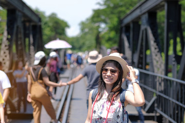 Young Woman traveling backpacker with hat, Asian traveler standing on the railway bridge over the river Kwai in Kanchanaburi, Thailand. history landmark and popular for tourist attractions