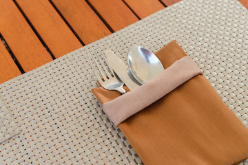 spoon, fork and knife with brown napkin on wooden table