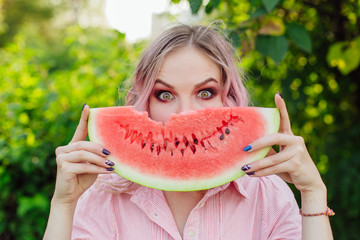 Beautiful young woman with pink hair holding juicy watermelon close to the face